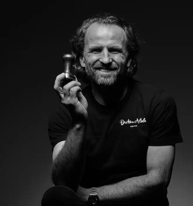 Smiling man holding a coffee tamper.