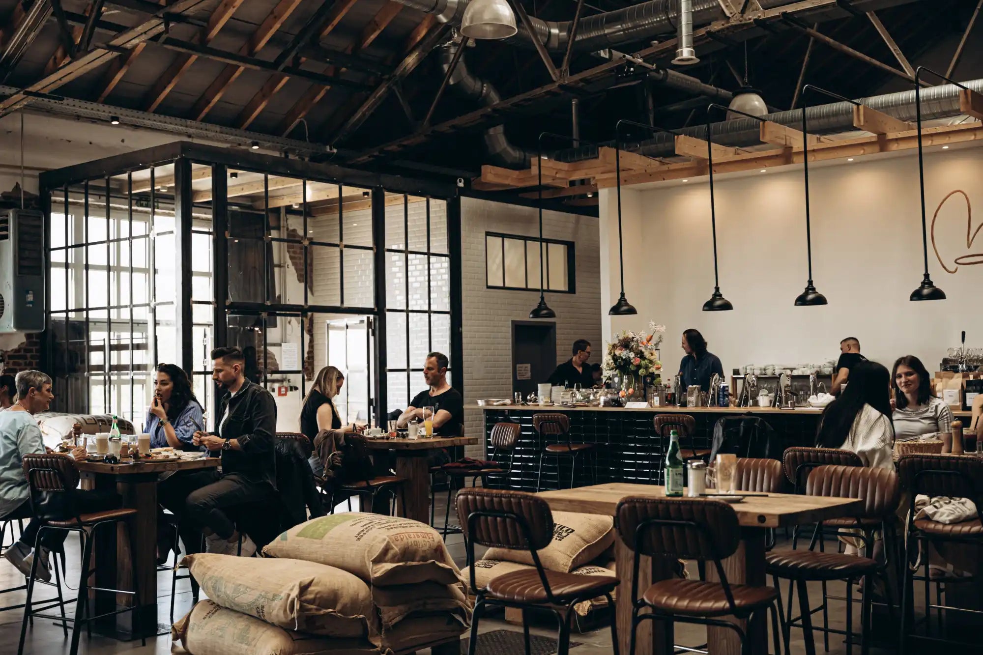 An interior shot of a spacious, modern coffee shop or restaurant with patrons seated at tables and a bar area.