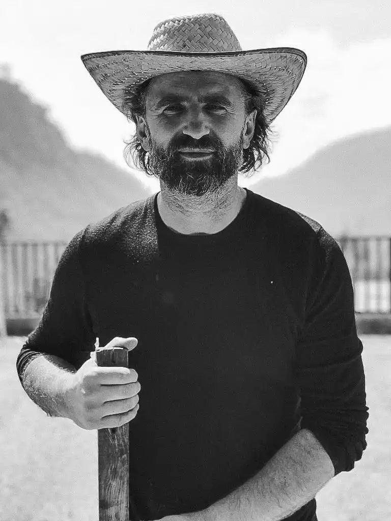 Man in straw hat holding wooden tool.