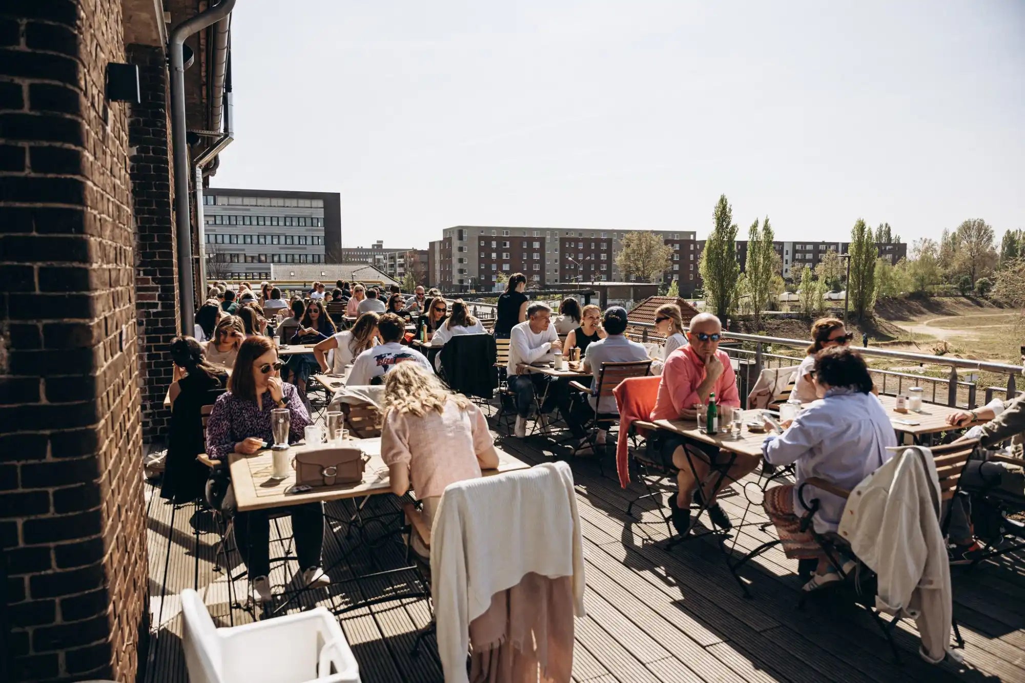 A bustling outdoor restaurant patio with many people seated at tables under bright sunlight.