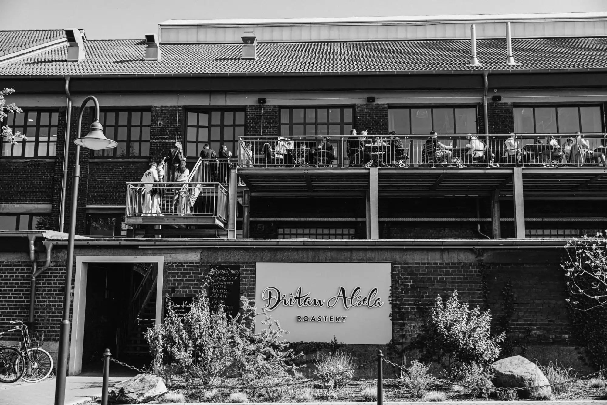 A two-story brick building with a balcony and outdoor seating, featuring a sign for a roastery.
